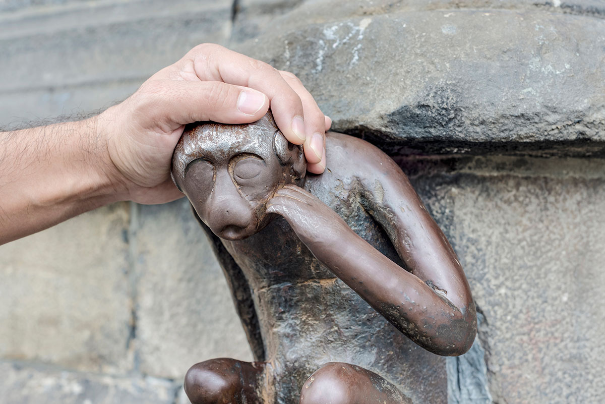 A hand petting a iron statue of a cute monkey